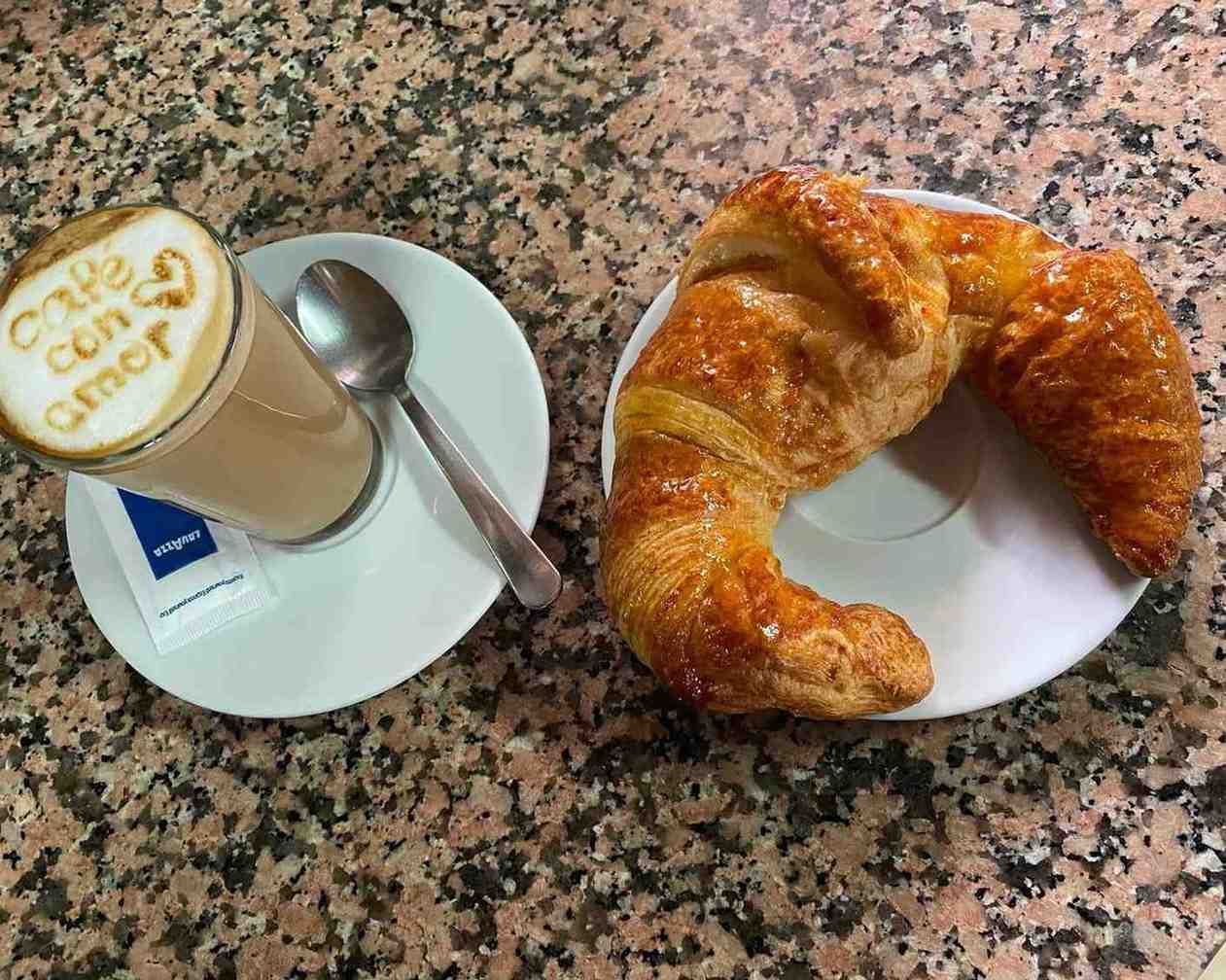 Café y un cruasán en platos blancos sobre una encimera moteada.