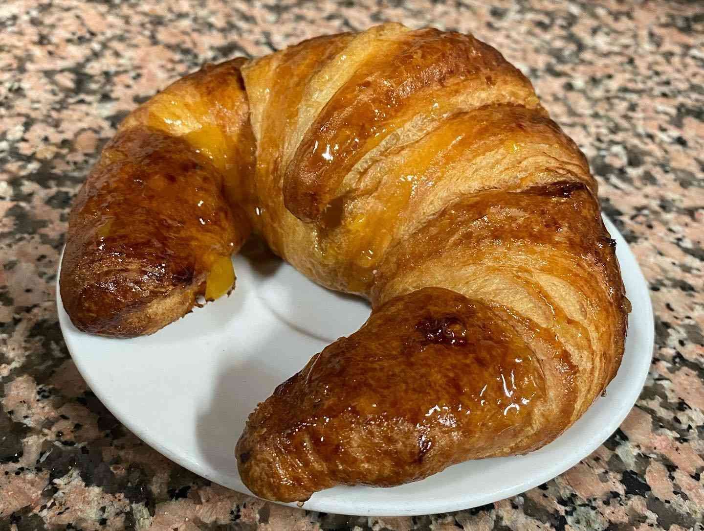 Croissant en un plato blanco con una corteza hojaldrada de color marrón dorado.