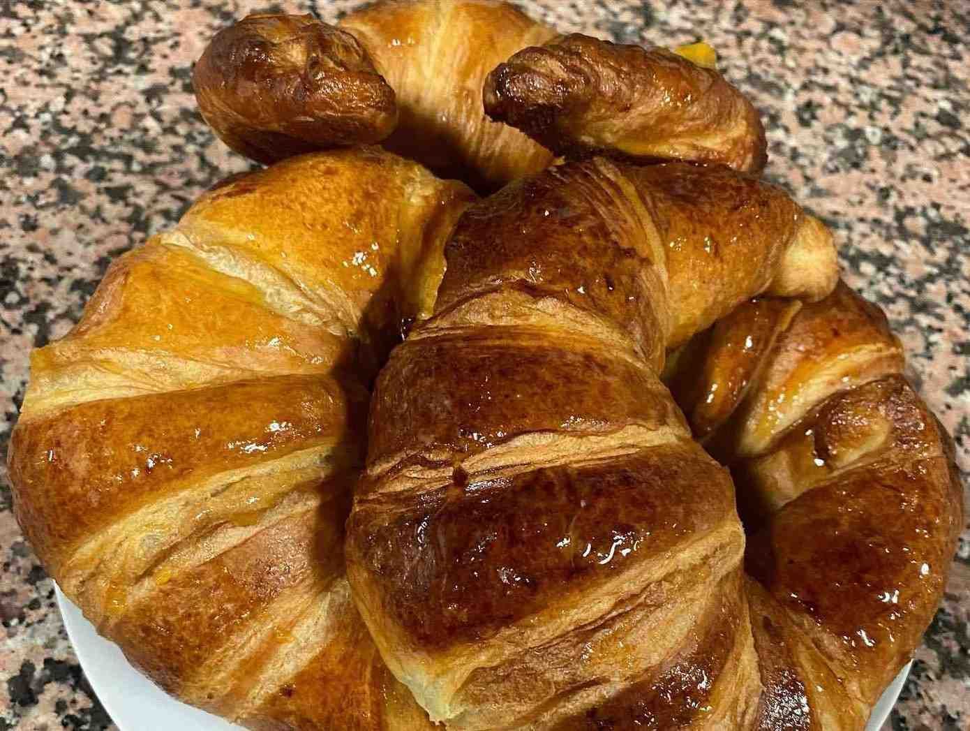 Variedad de croissants dorados apilados sobre una encimera moteada.