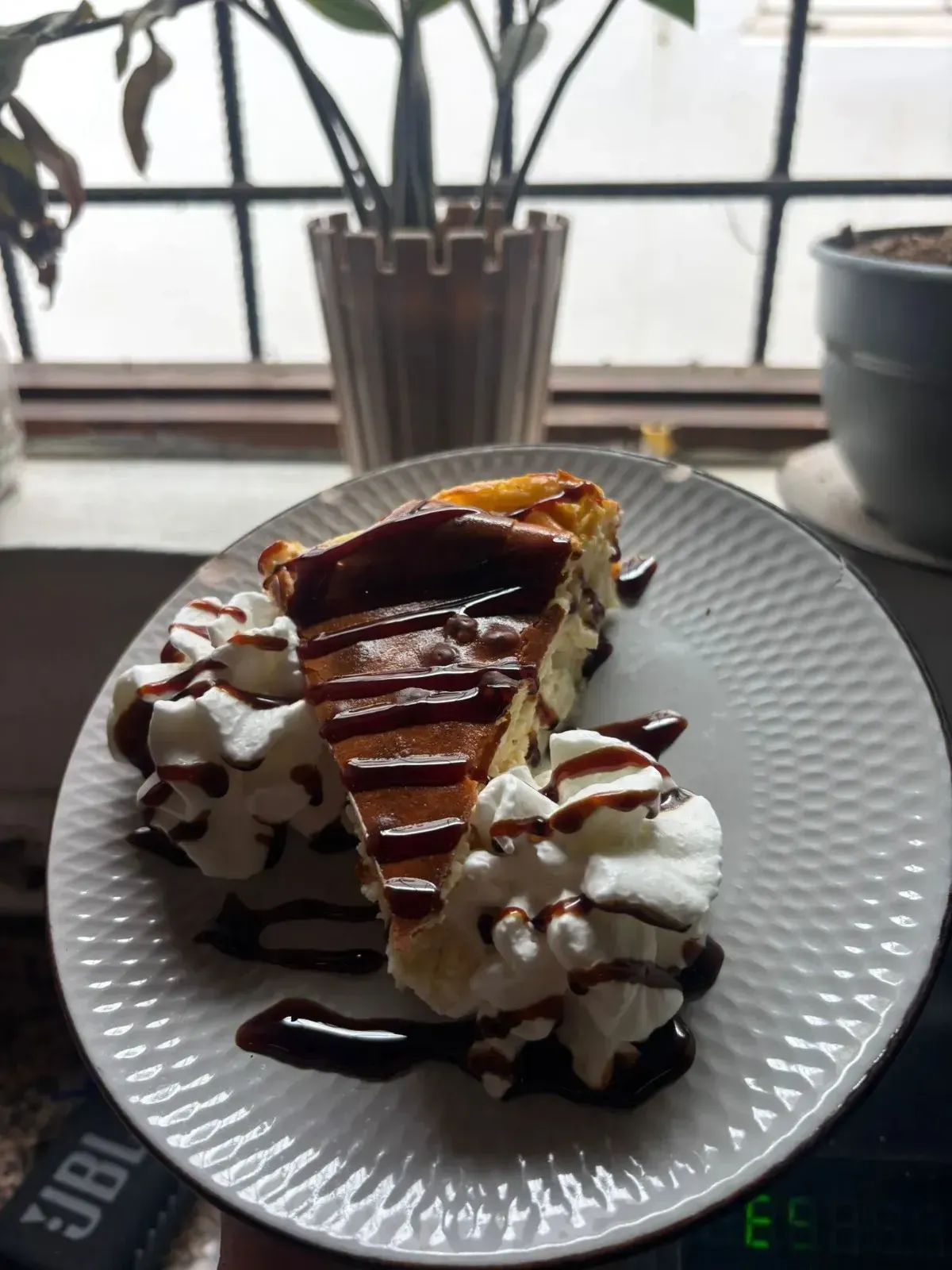 Crepe de postre con nata montada y sirope de chocolate en un plato blanco junto a una ventana.