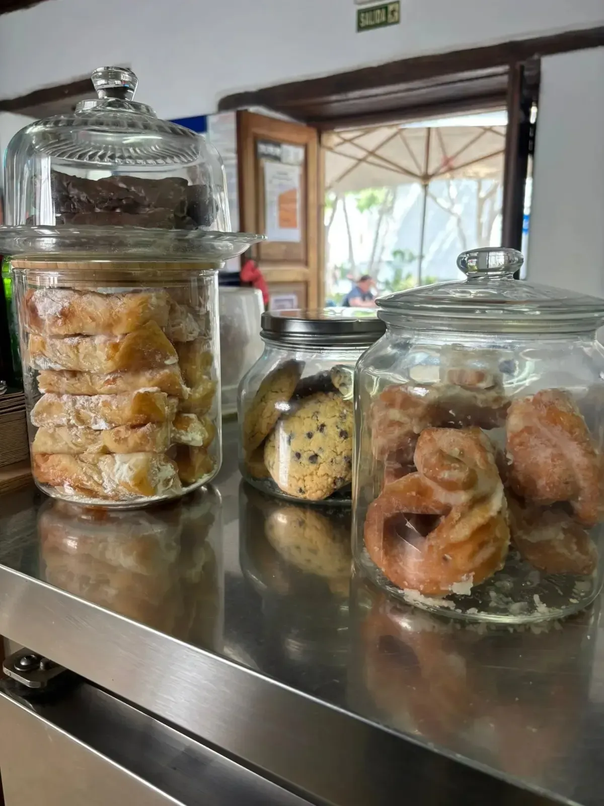 Frascos de vidrio con galletas y pasteles variados sobre la encimera de la cocina, cerca de una ventana.