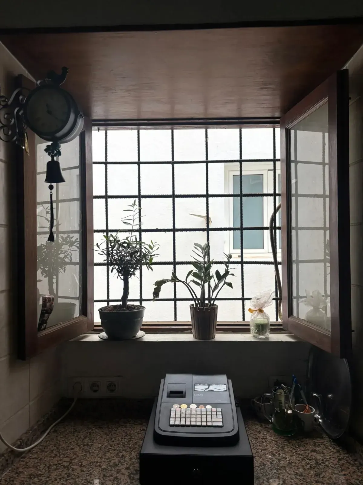 Un escritorio junto a una ventana con plantas en macetas y una máquina de escribir en una habitación pequeña.