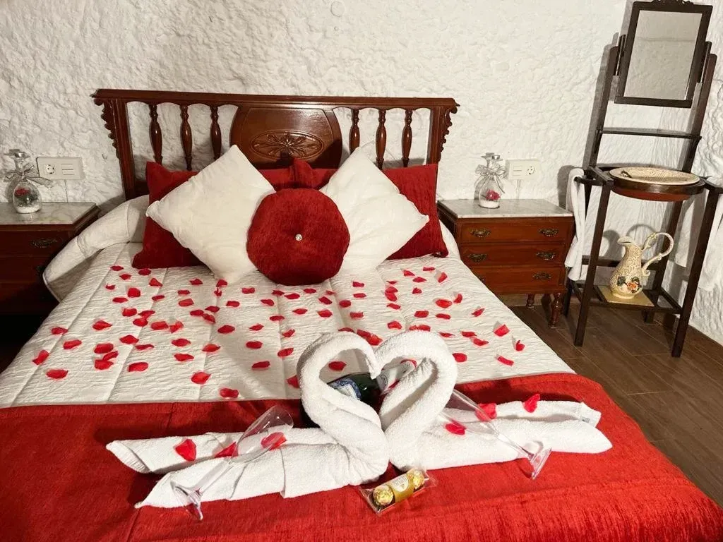 Dormitorio romántico con detalles en rojo, arte de toalla con forma de cisne y pétalos de rosa sobre una cama.