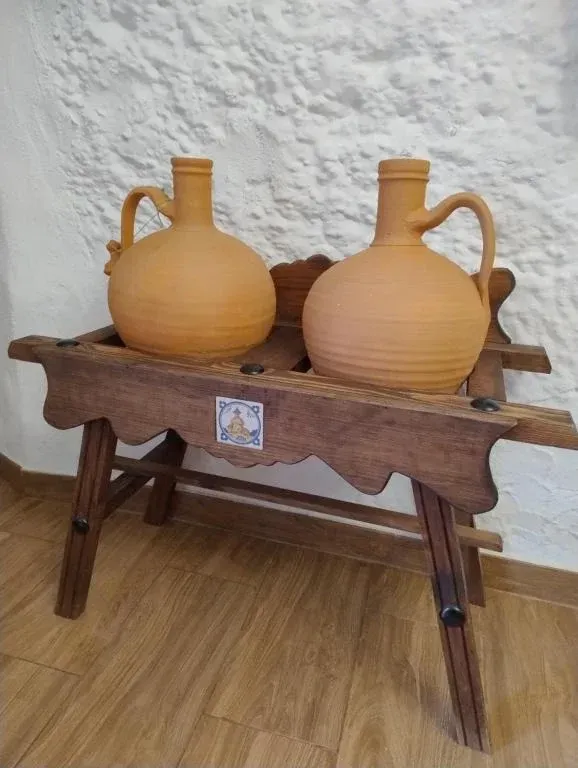 Dos jarras de terracota sobre una mesa de madera contra una pared blanca texturizada.