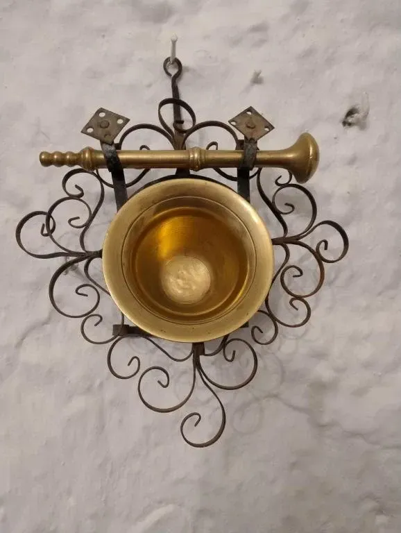 Mortero y mano de mortero de latón en soporte de hierro forjado ornamentado.