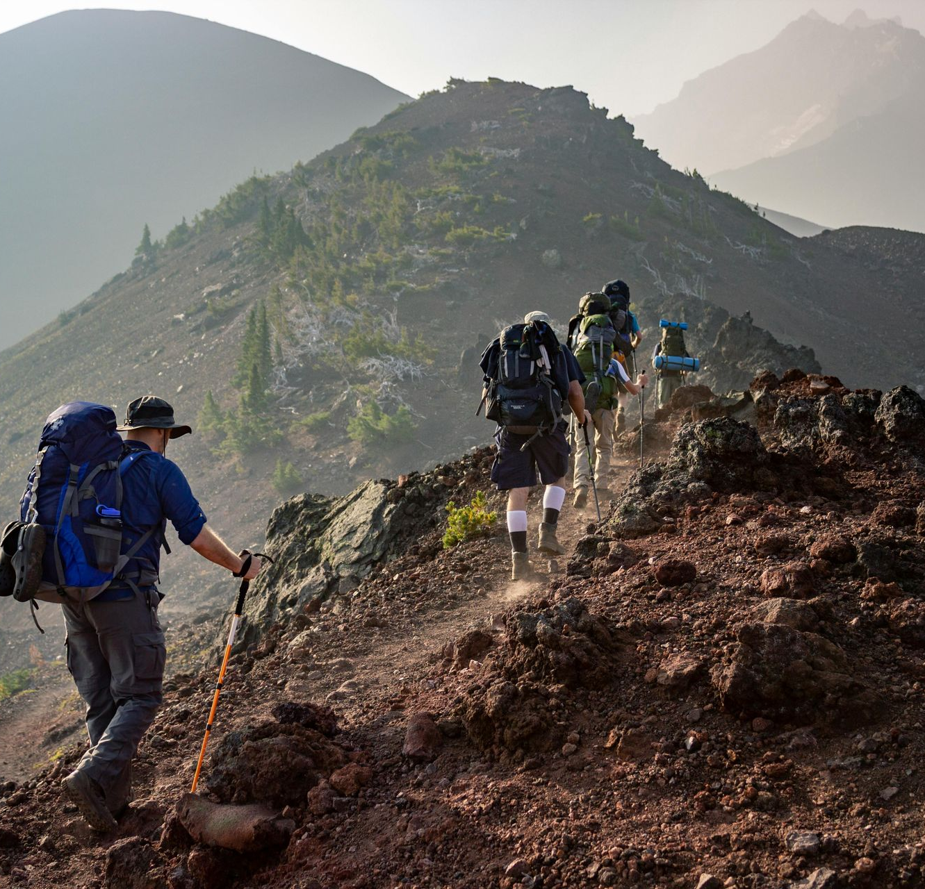 Los excursionistas ascienden por un sendero rocoso de montaña, cargando mochilas.