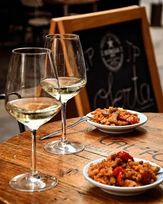 Sobre una mesa de madera hay dos copas de vino y dos platos de comida.