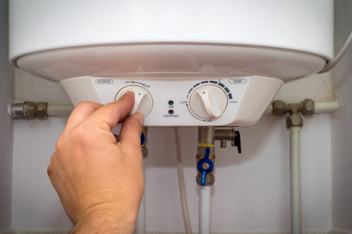 Perilla giratoria manual en un calentador de agua, electrodoméstico blanco en una pared blanca, con tuberías.
