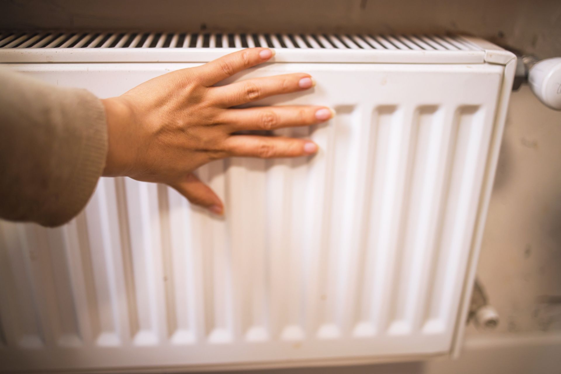 Mano tocando un radiador blanco, posiblemente probando su calor en el interior.