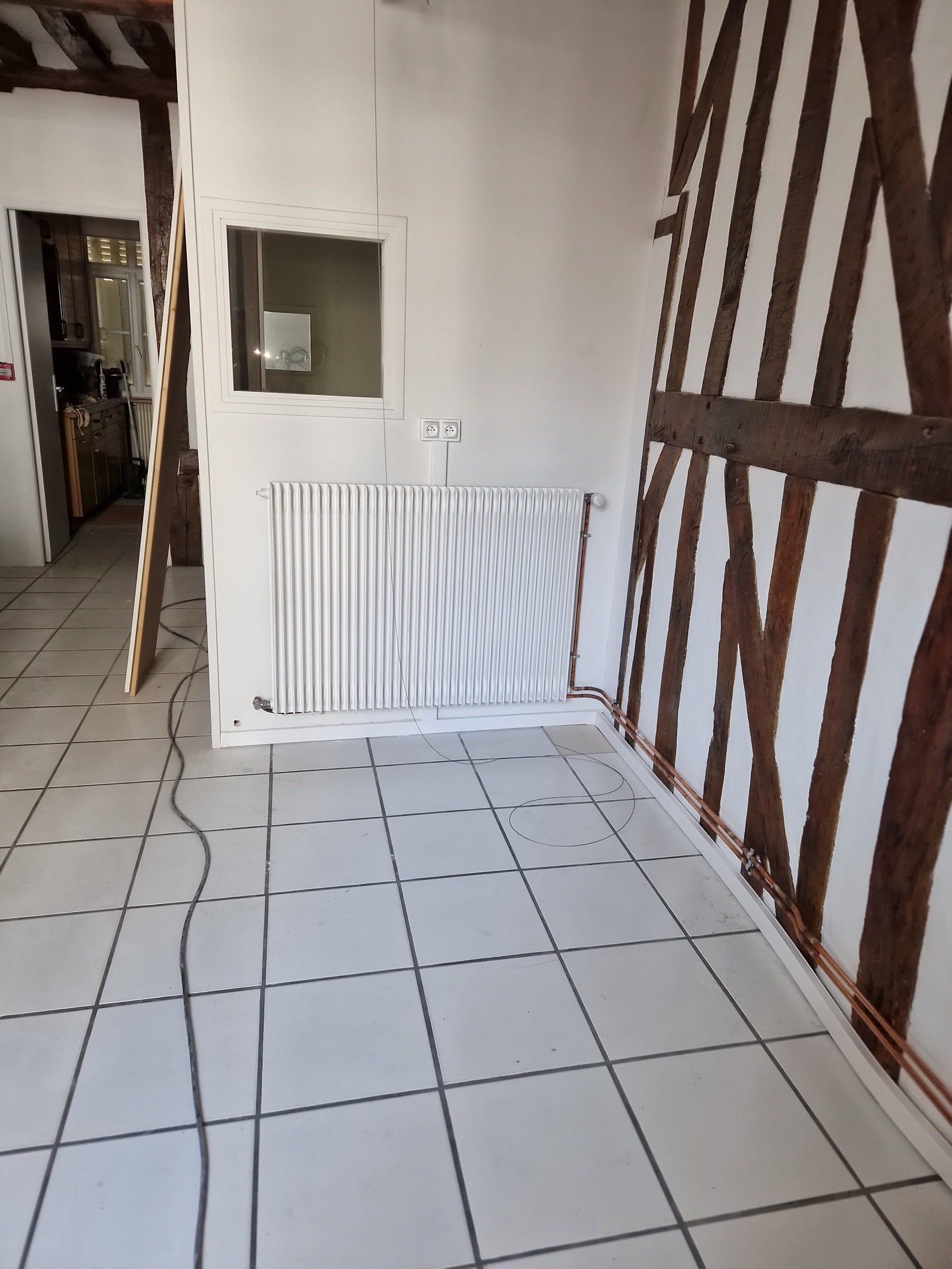 Radiateur blanc au mur dans une pièce avec du carrelage
