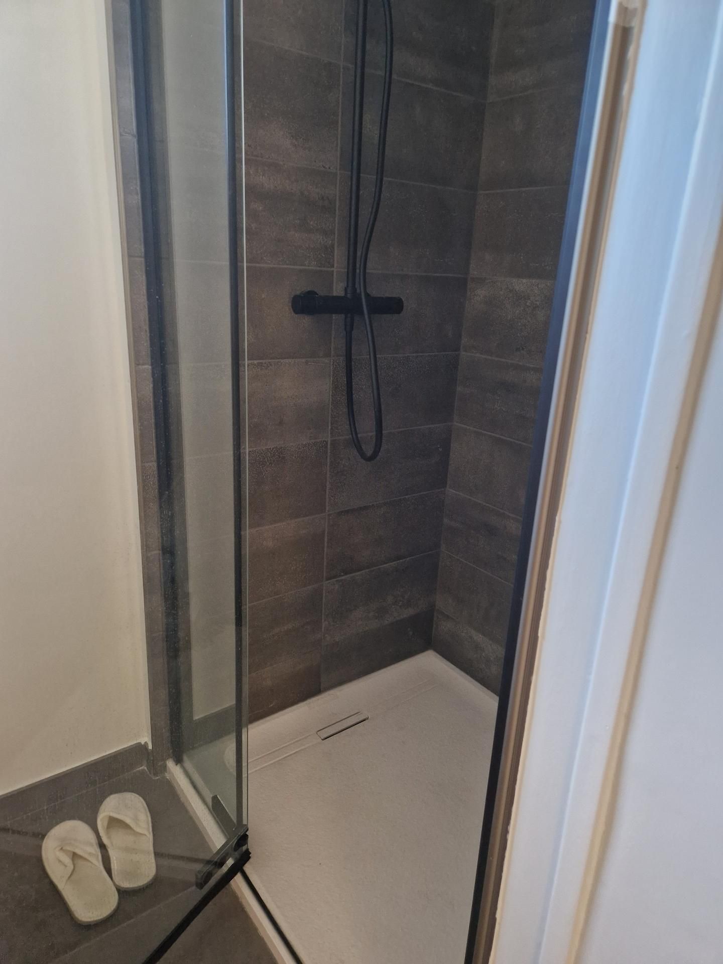 Coin douche rénovée avec un revêtement gris au mur et une vitre