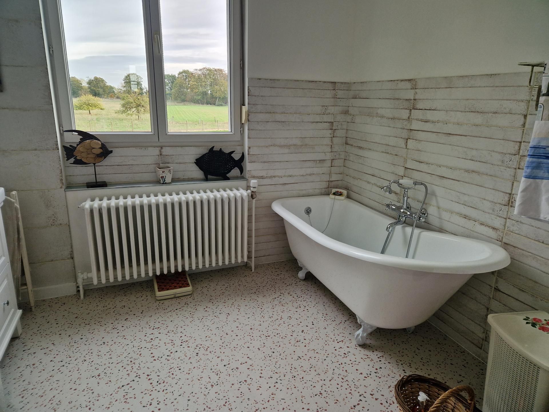 Salle de bains rénovée avec du lambris blanc au mur, une baignoire et un radiateur