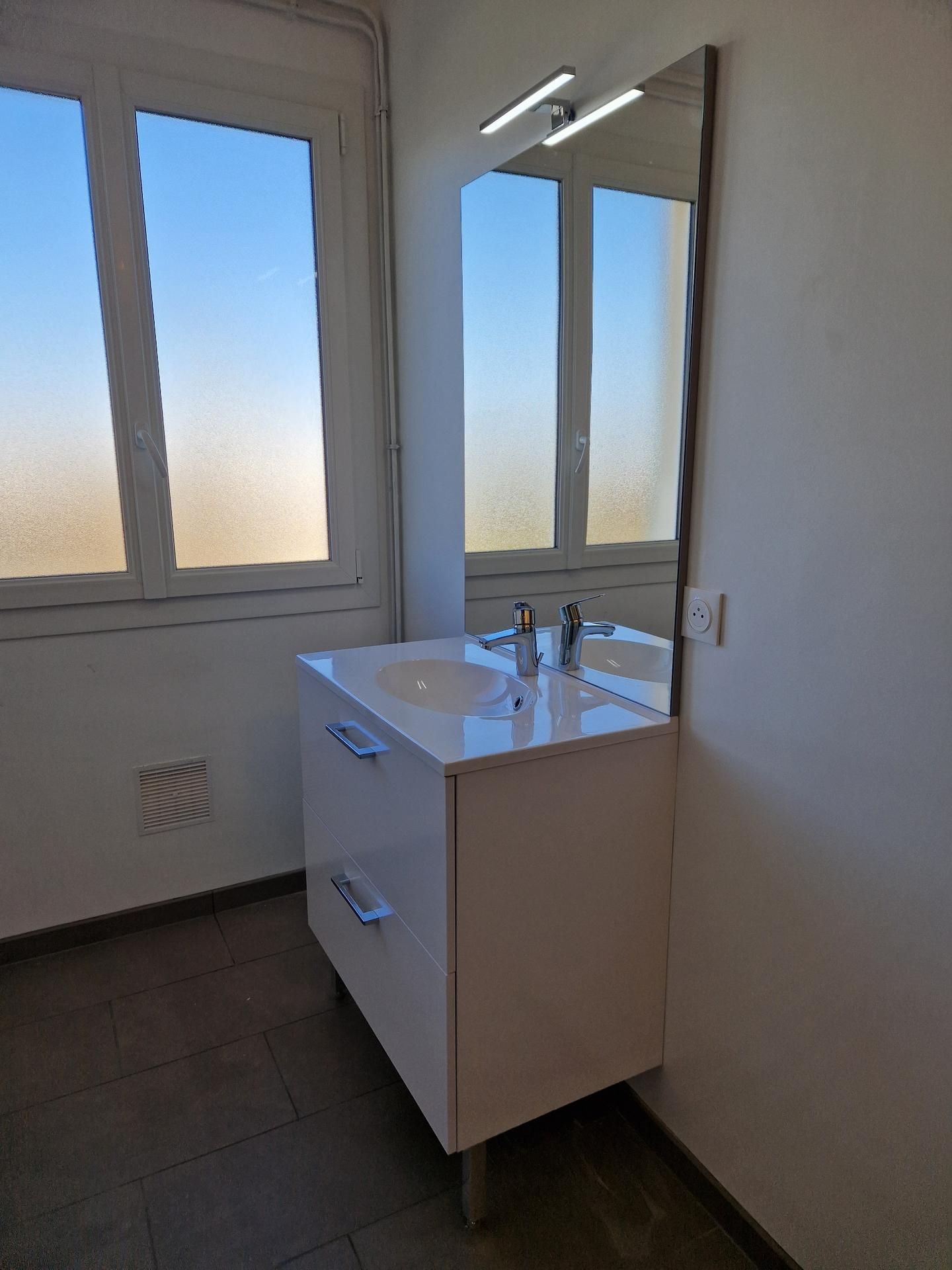 Meuble de salle de bains clair avec un lavabo, un miroir et une fenêtre fermée