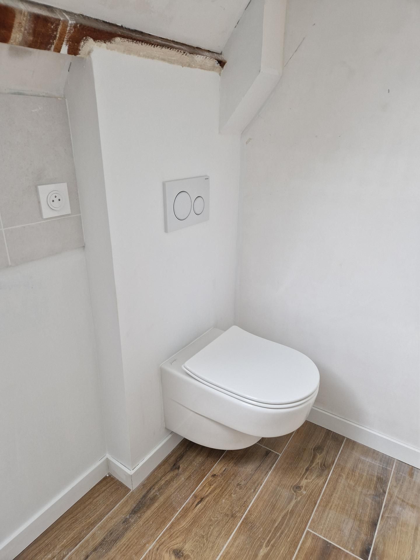 WC blanc fermé avec une chasse en hauteur et une prise électrique au mur