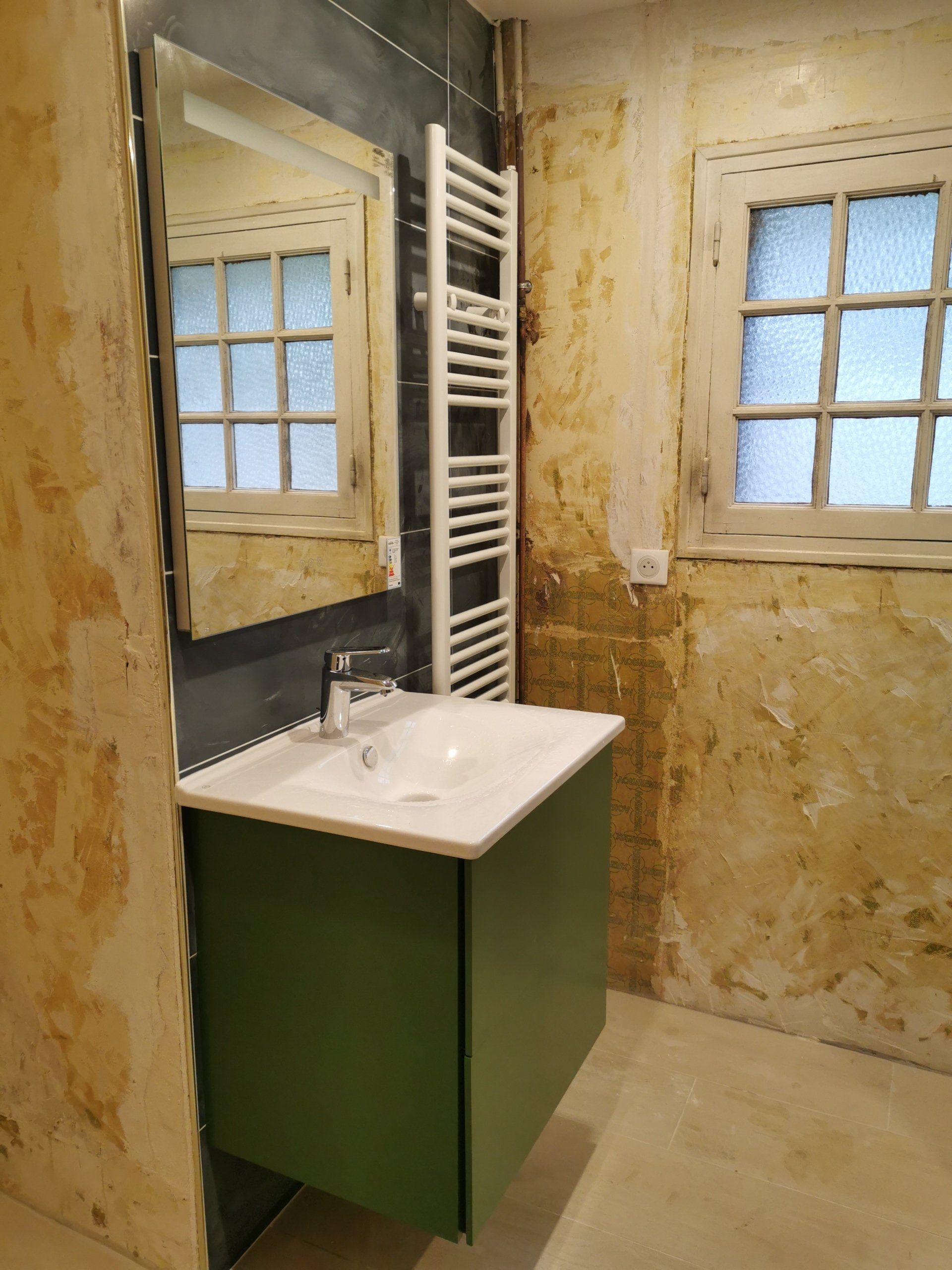 Salle de bains en cours de rénovation avec un lavabo, un miroir et un sèche-serviettes