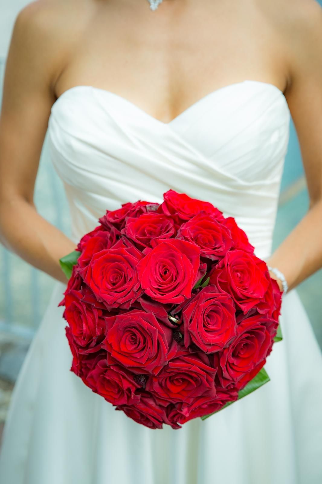 Eine Braut in einem weißen Kleid hält einen Strauß roter Rosen in der Hand.