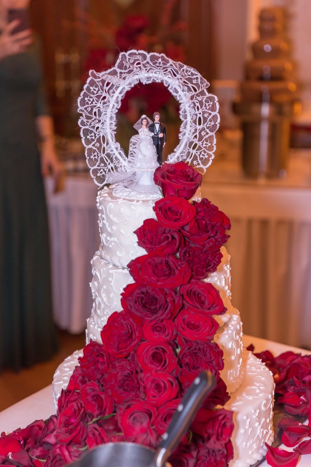 Eine Hochzeitstorte mit roten Rosen und einer Braut- und Bräutigamfigur obendrauf.
