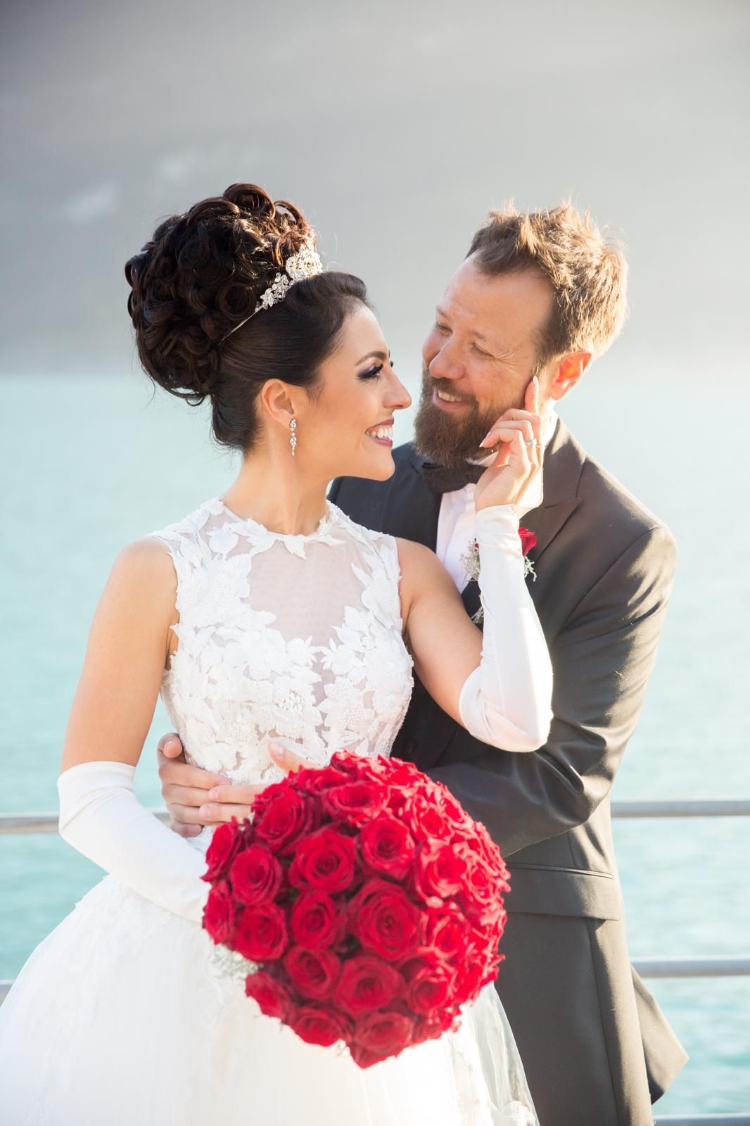 Eine Braut und ein Bräutigam posieren für ein Foto, während die Braut einen Strauß roter Rosen hält.