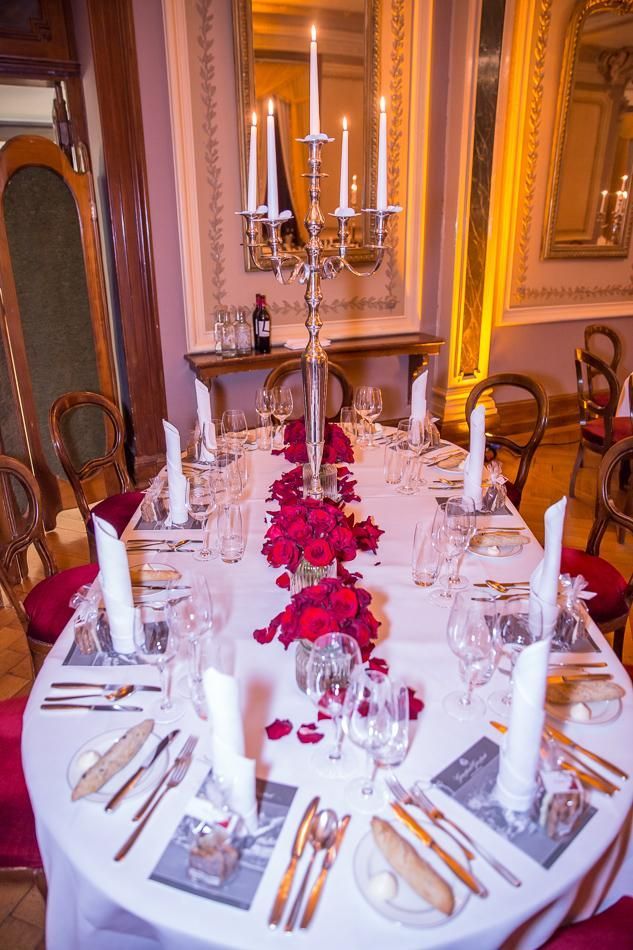 Ein langer Tisch mit einem Kerzenleuchter und roten Blumen darauf.