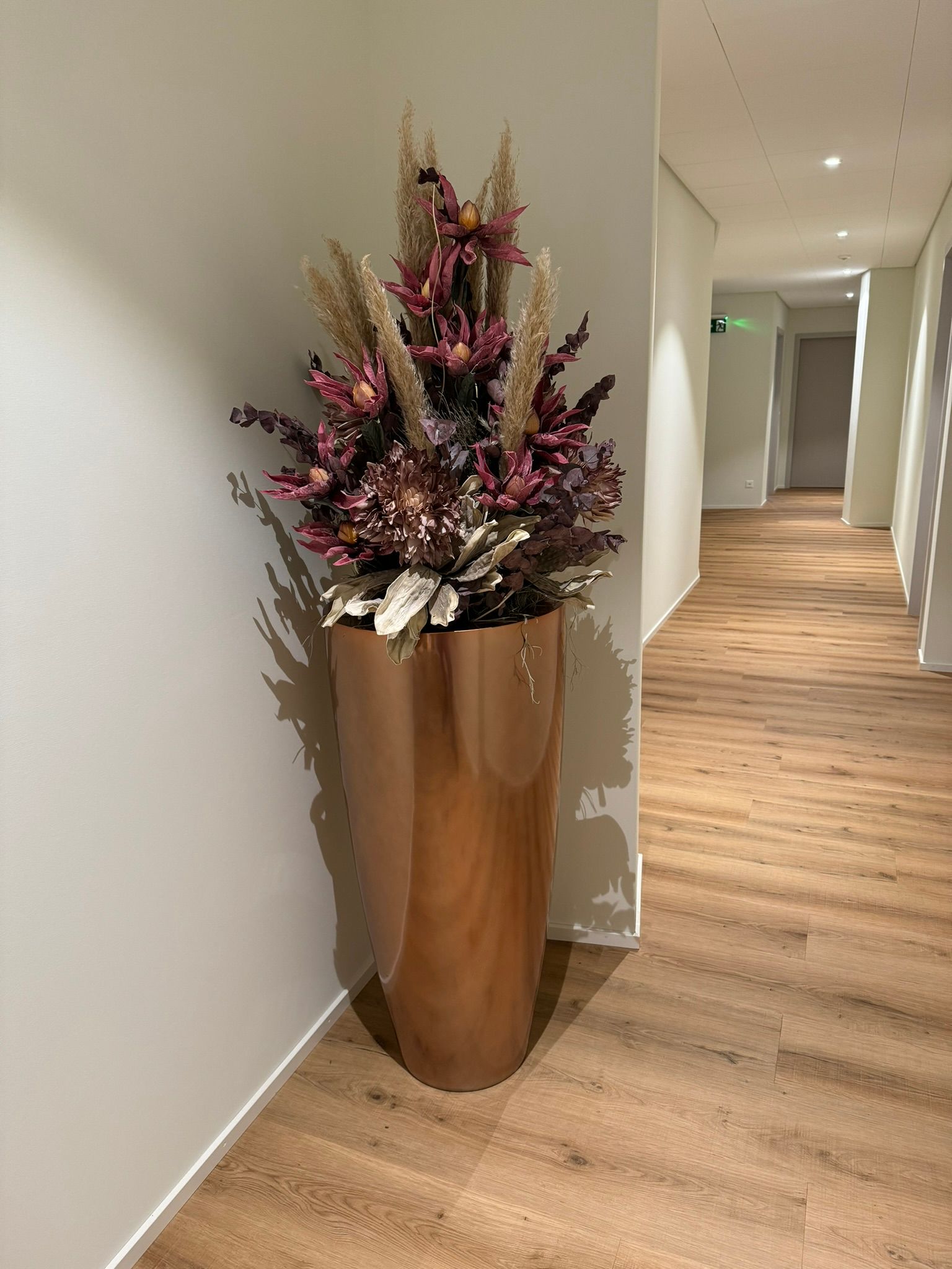 In einem Flur steht eine große Vase voller Blumen.