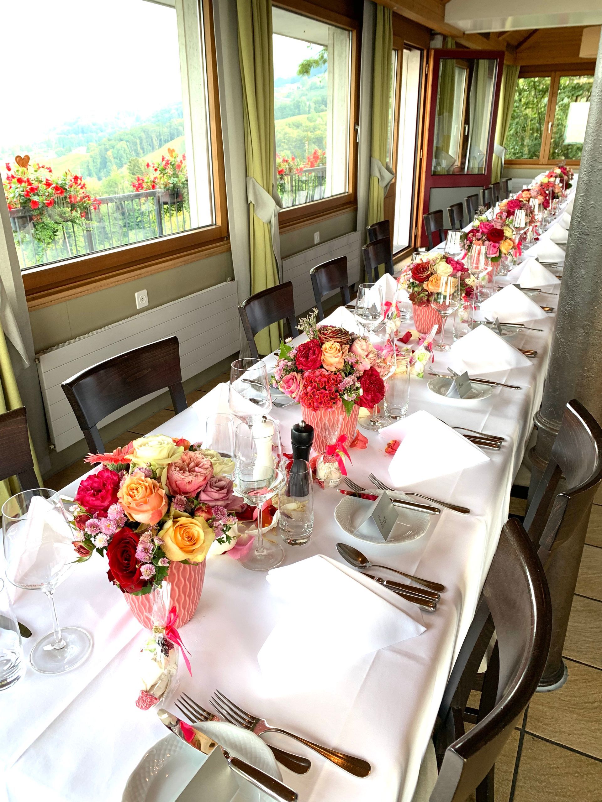 Ein langer Tisch mit Tellern, Besteck und Blumen darauf.