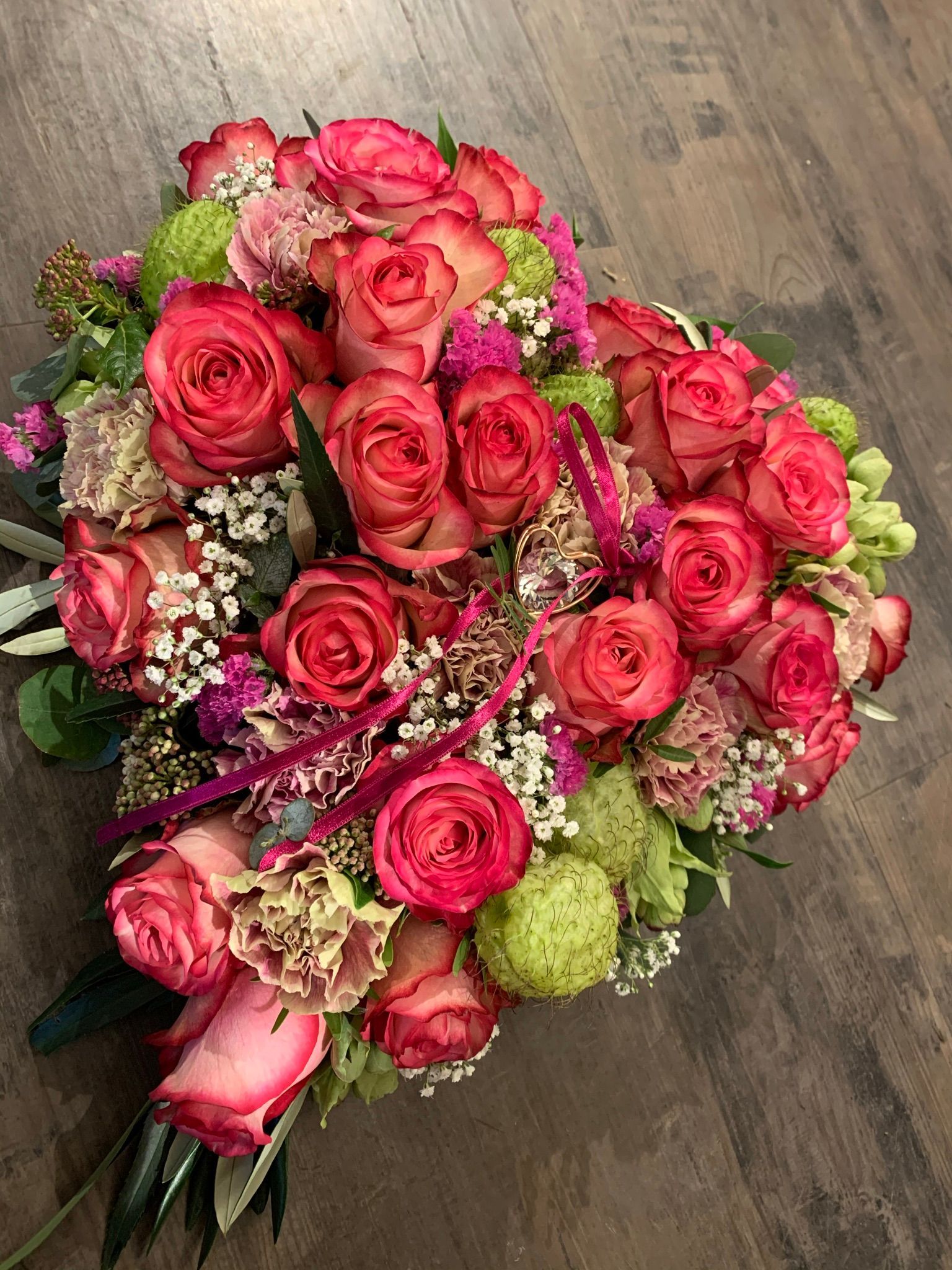 Auf einem Holztisch steht ein Strauß rosa Rosen und anderer Blumen.