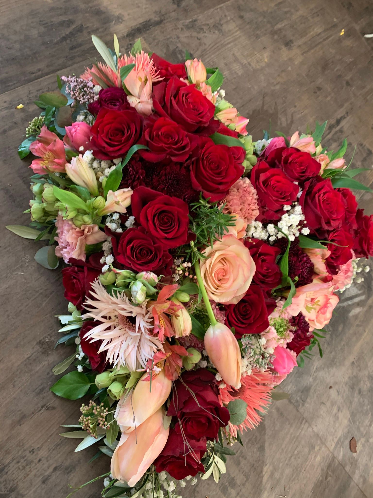 Auf einem Holztisch steht ein herzförmiger Blumenstrauß.