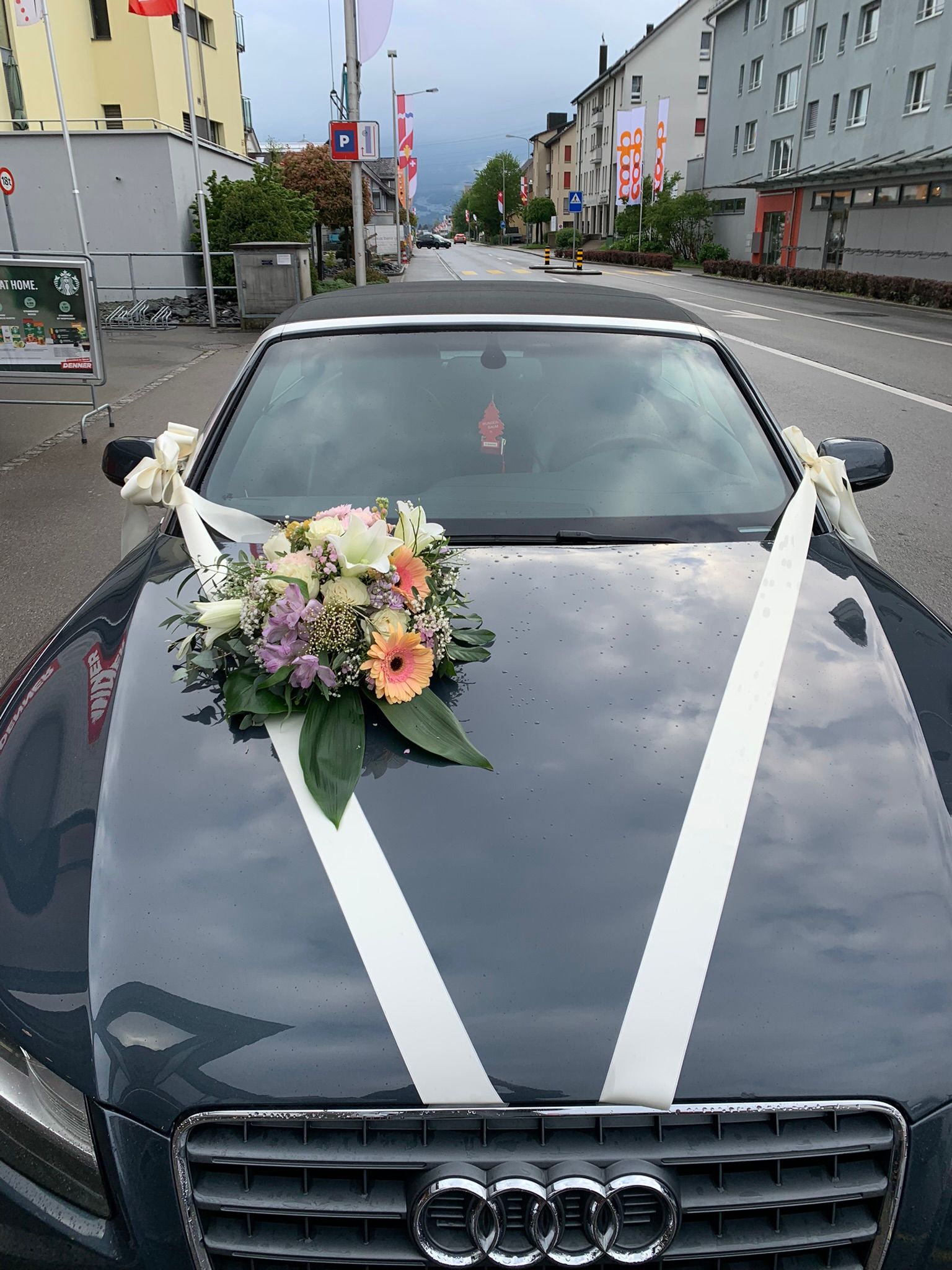 Ein schwarzes Auto mit Blumen auf der Motorhaube steht am Straßenrand.