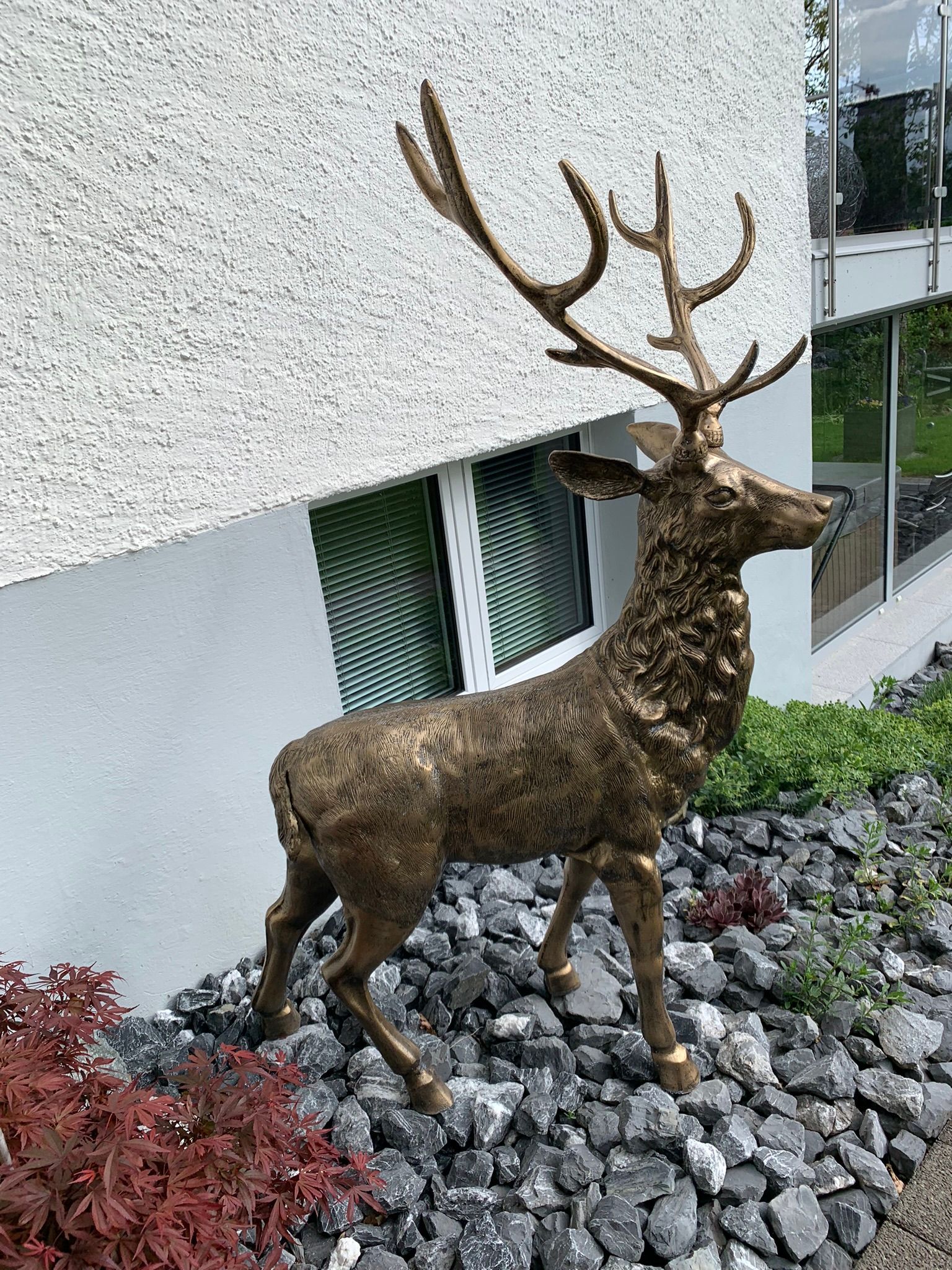 Eine bronzene Hirschstatue, die auf Felsen vor einem Gebäude steht.
