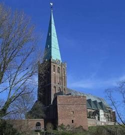 Auf einem Hügel steht eine große Backsteinkirche mit grünem Turm.