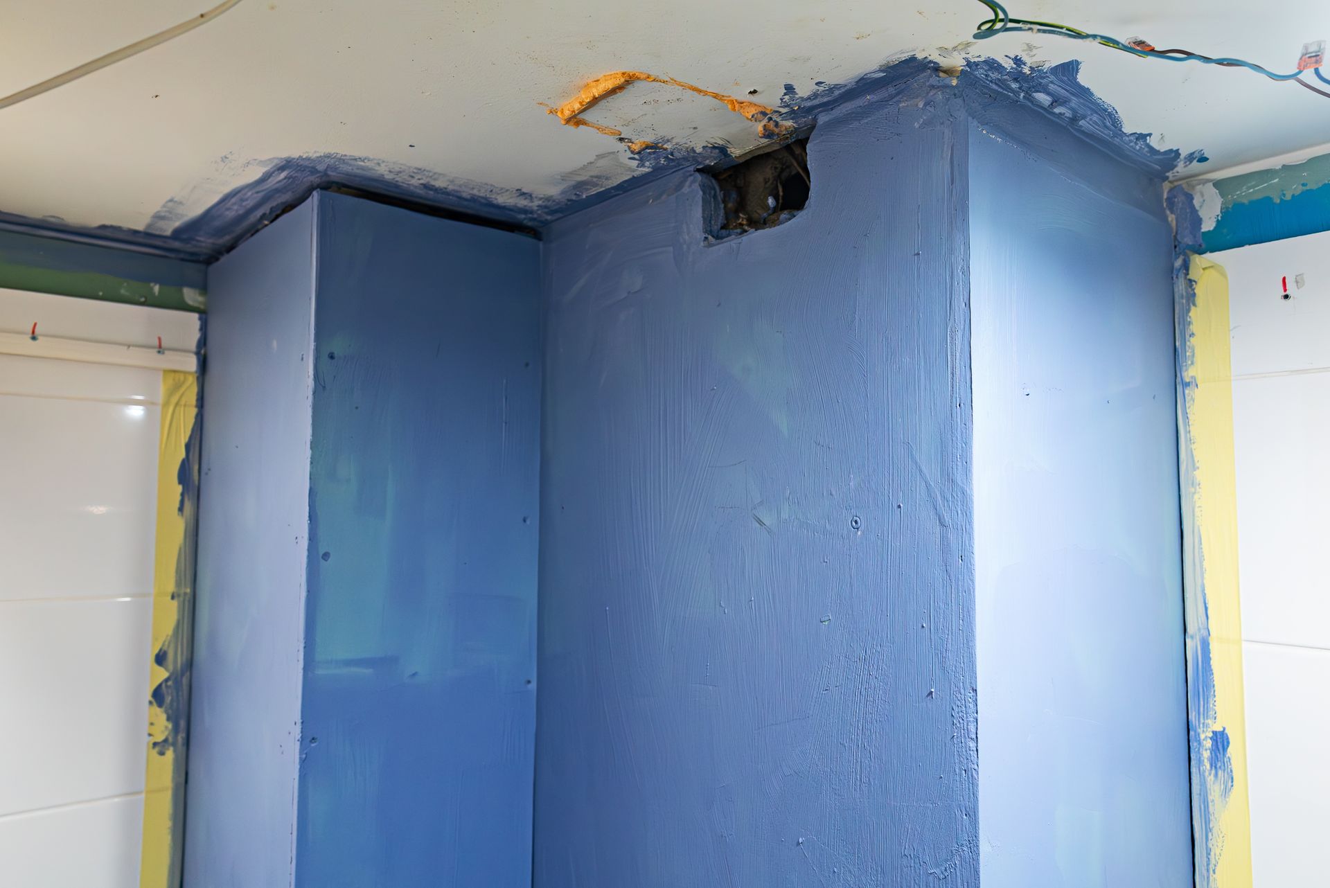 Murs d'angle peints en bleu dans une pièce, avec un trou dans le plafond et des bords non finis.