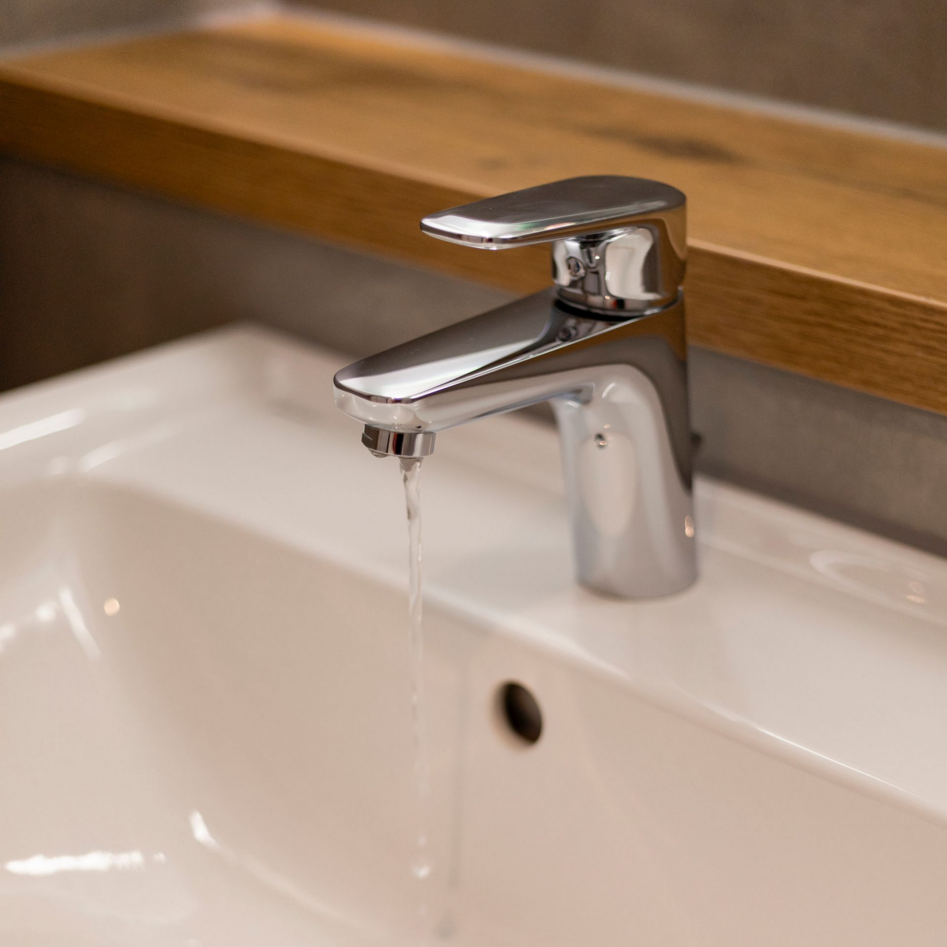 Robinet chromé avec eau courante dans un lavabo blanc. Étagère marron clair au-dessus.