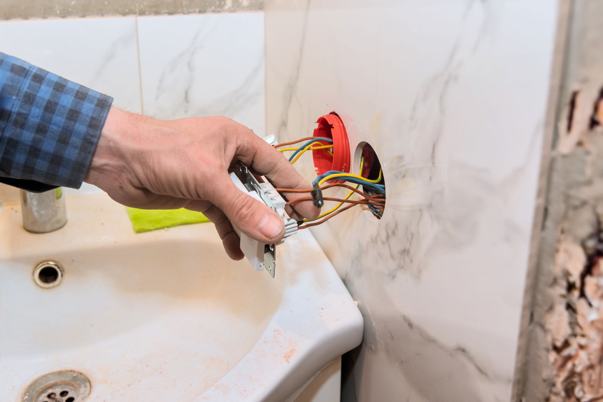 Installation manuelle d'une prise électrique près d'un lavabo de salle de bains, avec des fils exposés.