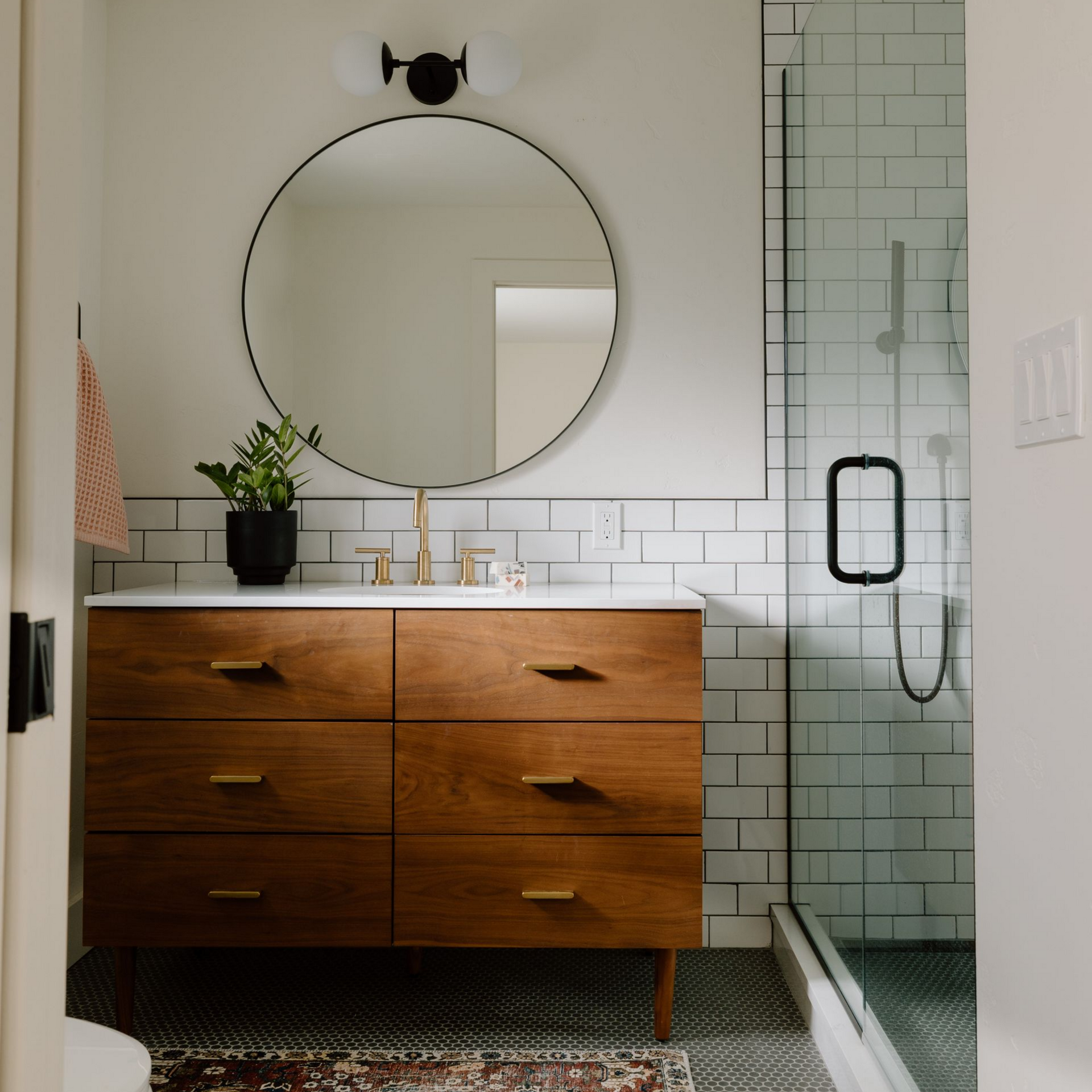 Salle de bains avec meuble lavabo en bois, miroir rond et douche en verre. Carrelage blanc style métro.
