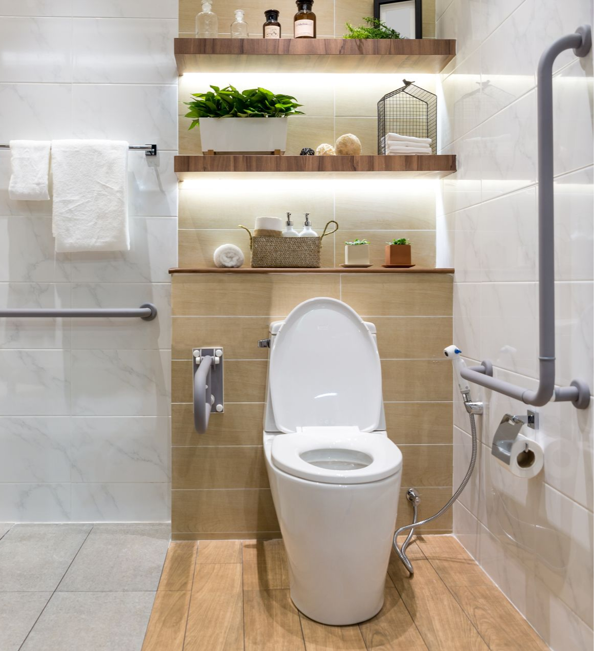 Salle de bains avec toilettes, étagères et barres d'appui. Tons blancs, beige et marron. Conçue pour l'accessibilité et le confort.