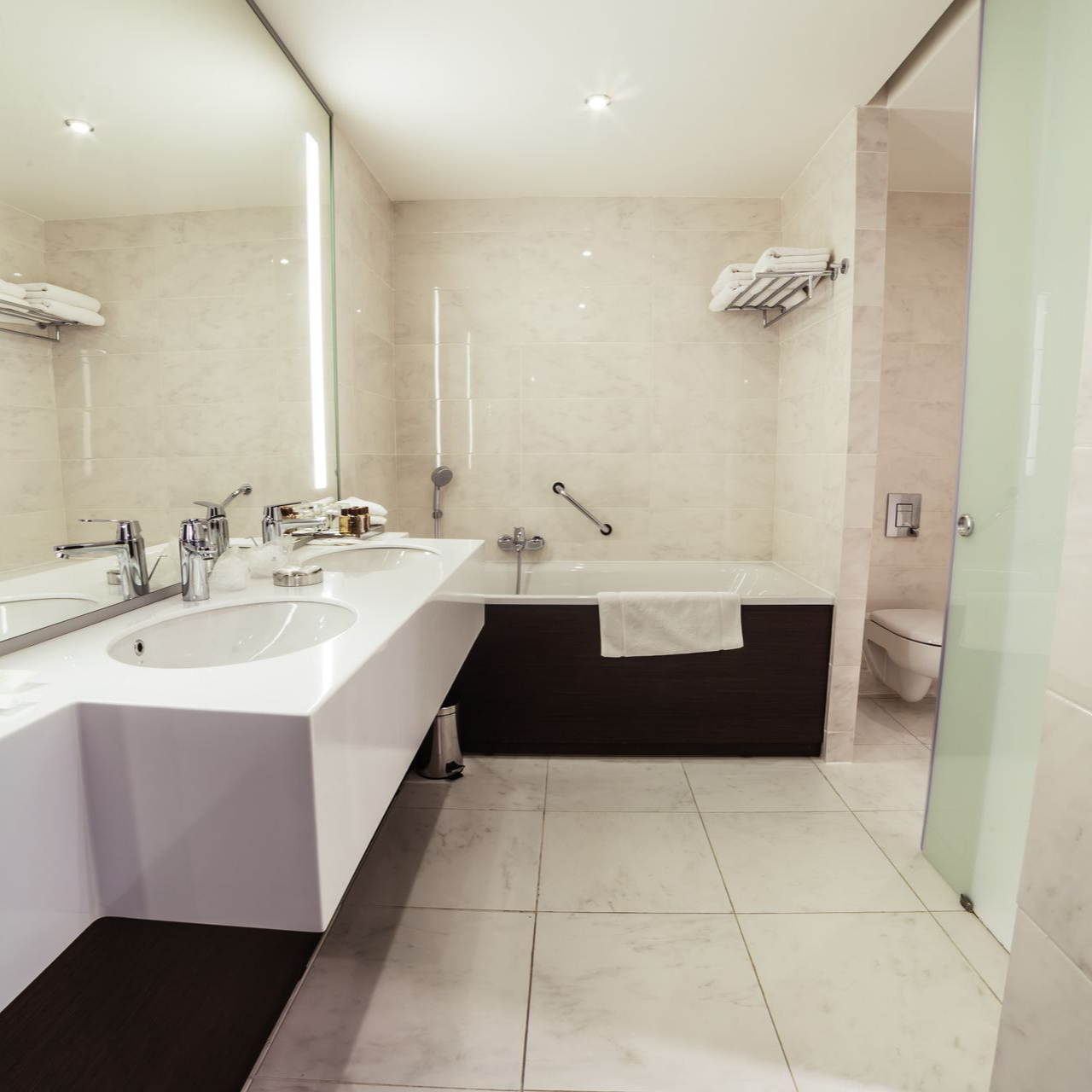 Salle de bains d'hôtel moderne avec vanité blanche, baignoire et douche.