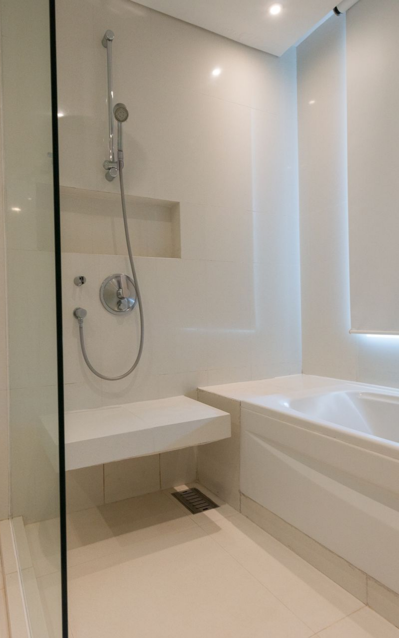 Salle de bains blanche et moderne avec douche, banc intégré et baignoire. La pièce est propre et lumineuse.