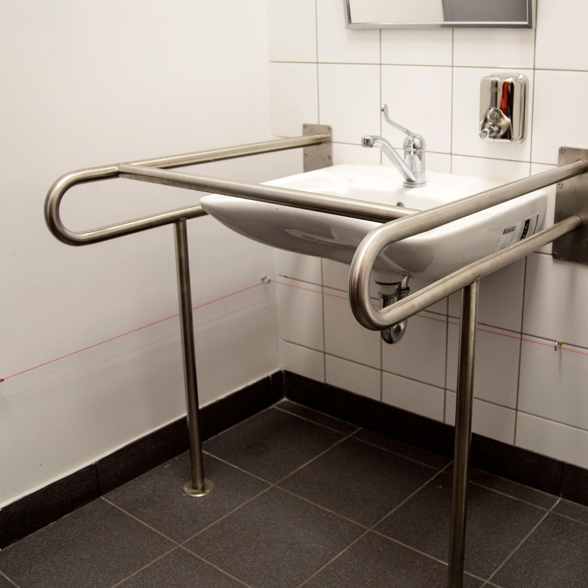 Évier en acier inoxydable avec barres d'appui accessibles dans des toilettes publiques.