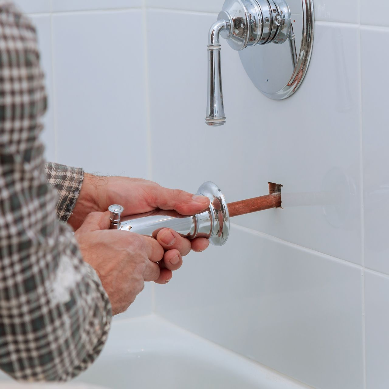 Personne installant une poignée de robinet dans une salle de bains carrelée blanche.