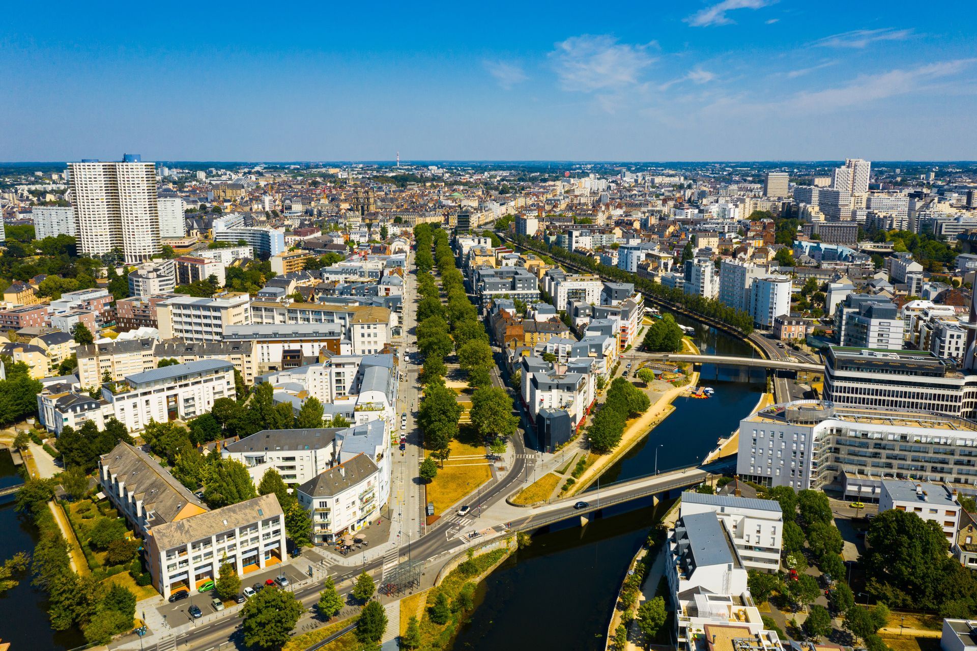 Vue aérienne d'une ville avec une rivière, des ponts et des bâtiments sous un ciel bleu.