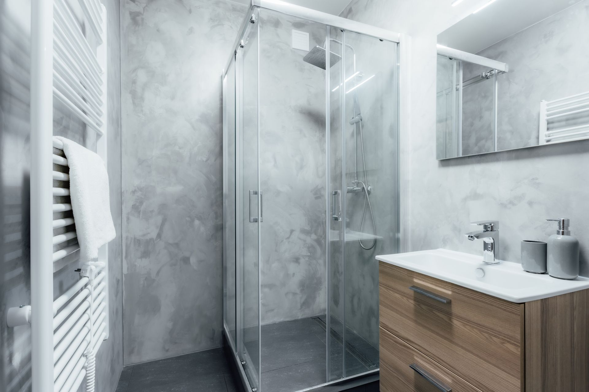 Salle de bains moderne avec douche en verre, meuble lavabo en bois et sèche-serviettes. Murs gris.