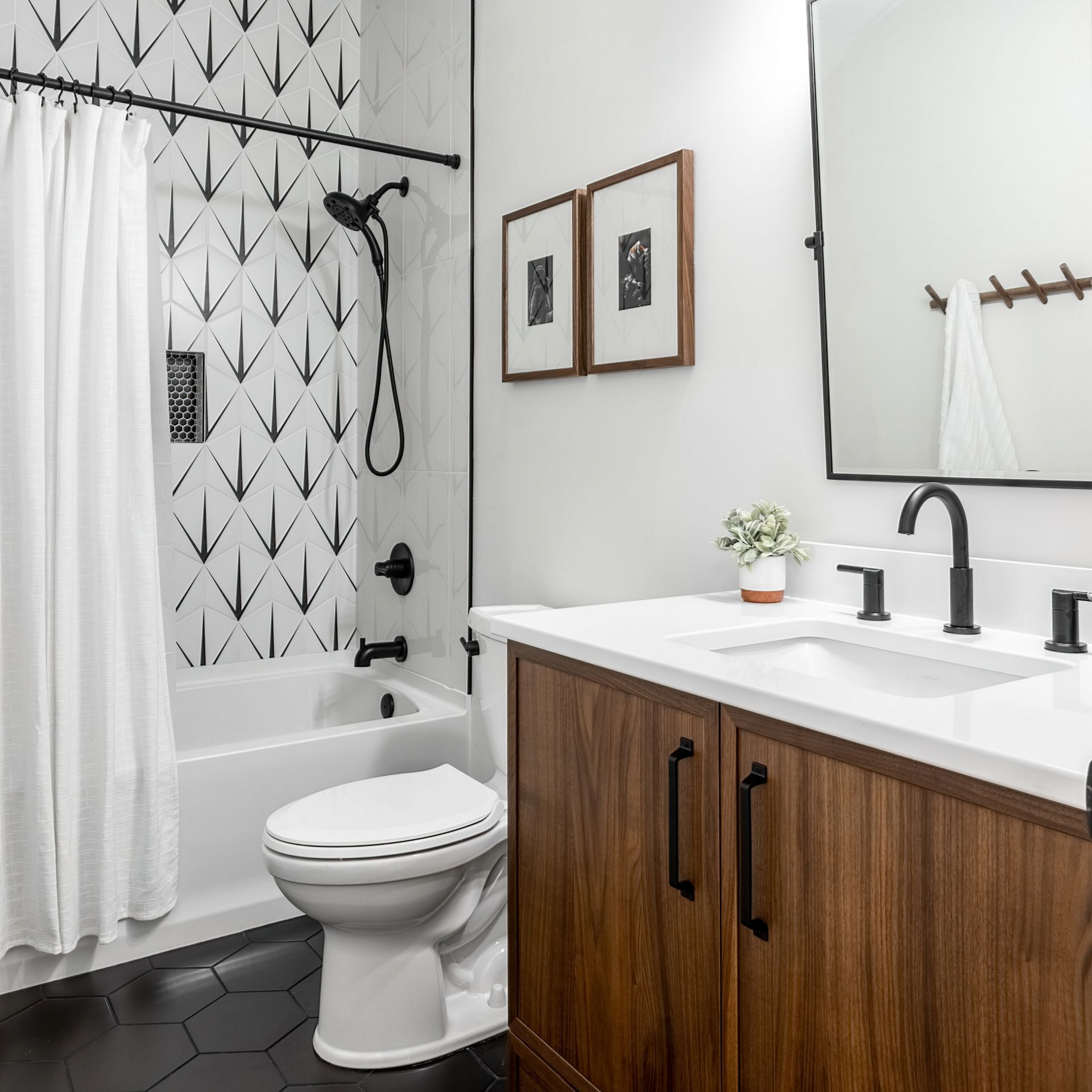 Salle de bains moderne avec murs blancs, vanité en bois, luminaires noirs et douche en carrelage à motifs.