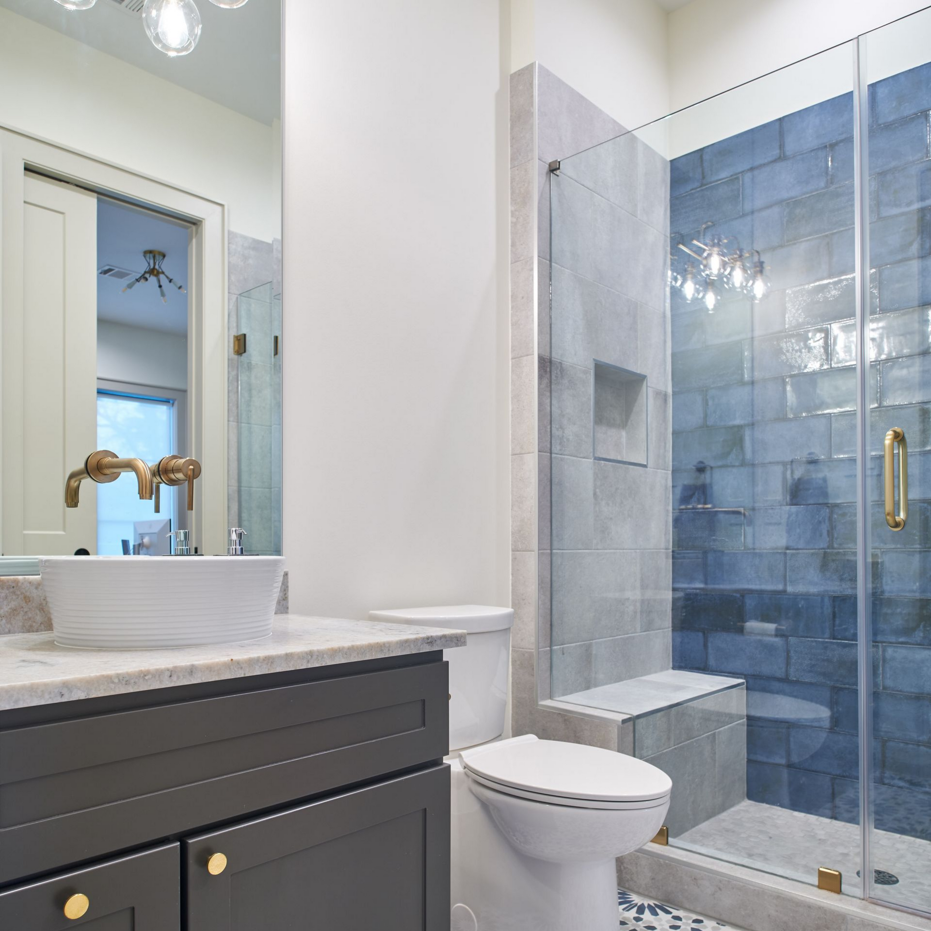 Salle de bains avec vanité grise, lavabo blanc, douche carrelée bleue et toilettes blanches.
