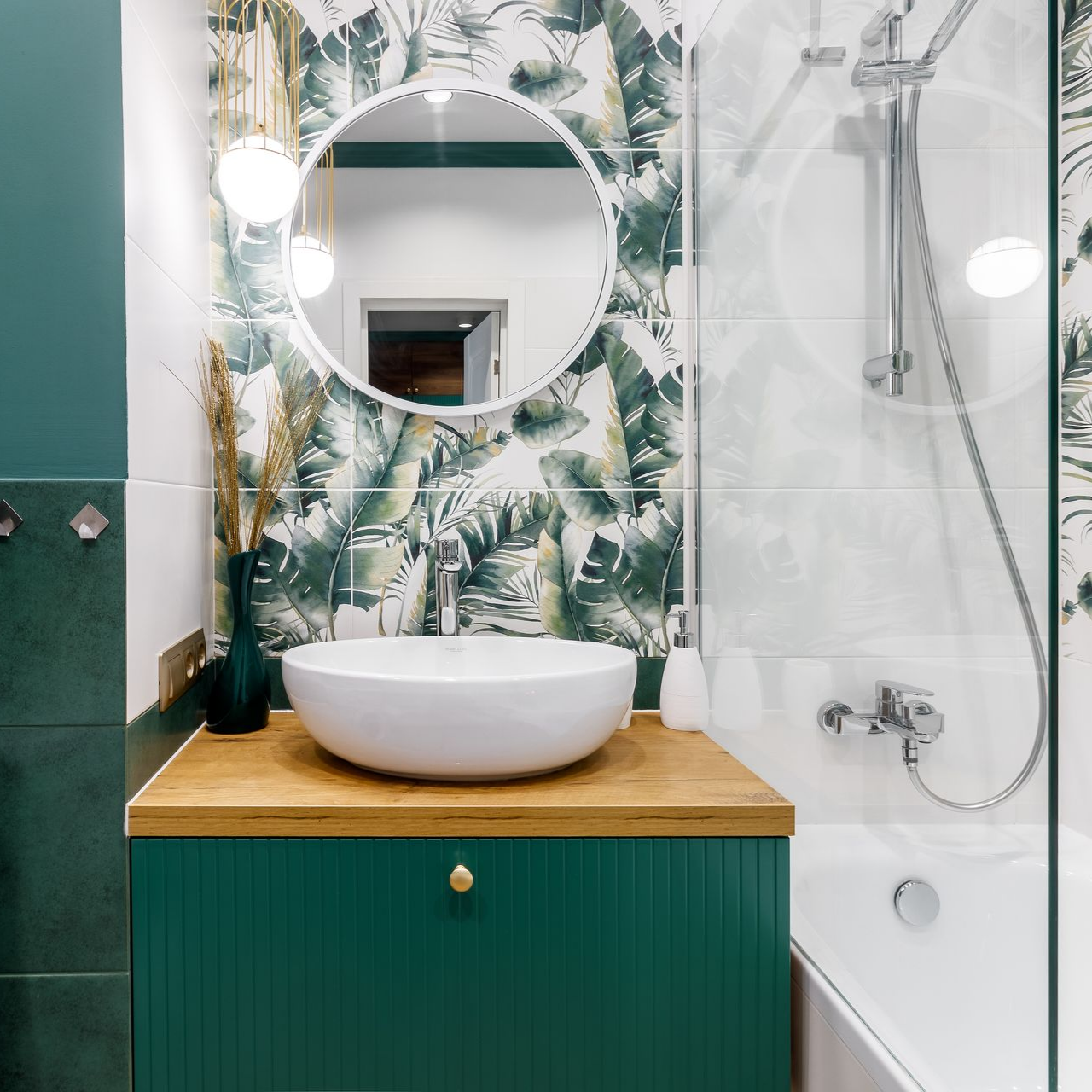 Salle de bains verte et blanche avec papier peint botanique, un miroir rond et un lavabo.