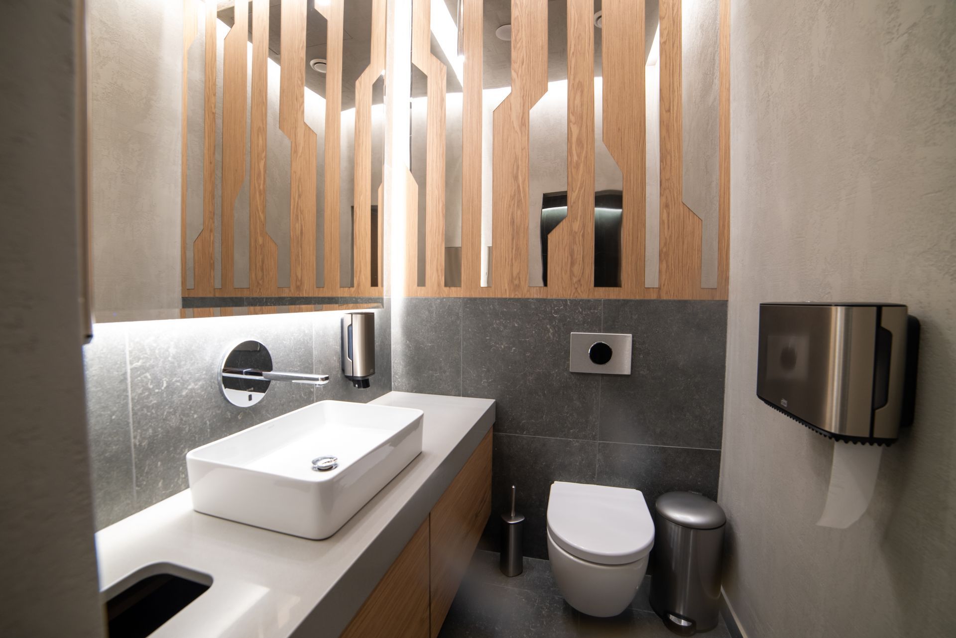 Toilettes modernes avec lavabo blanc, toilettes et boiseries. Murs et sol gris.