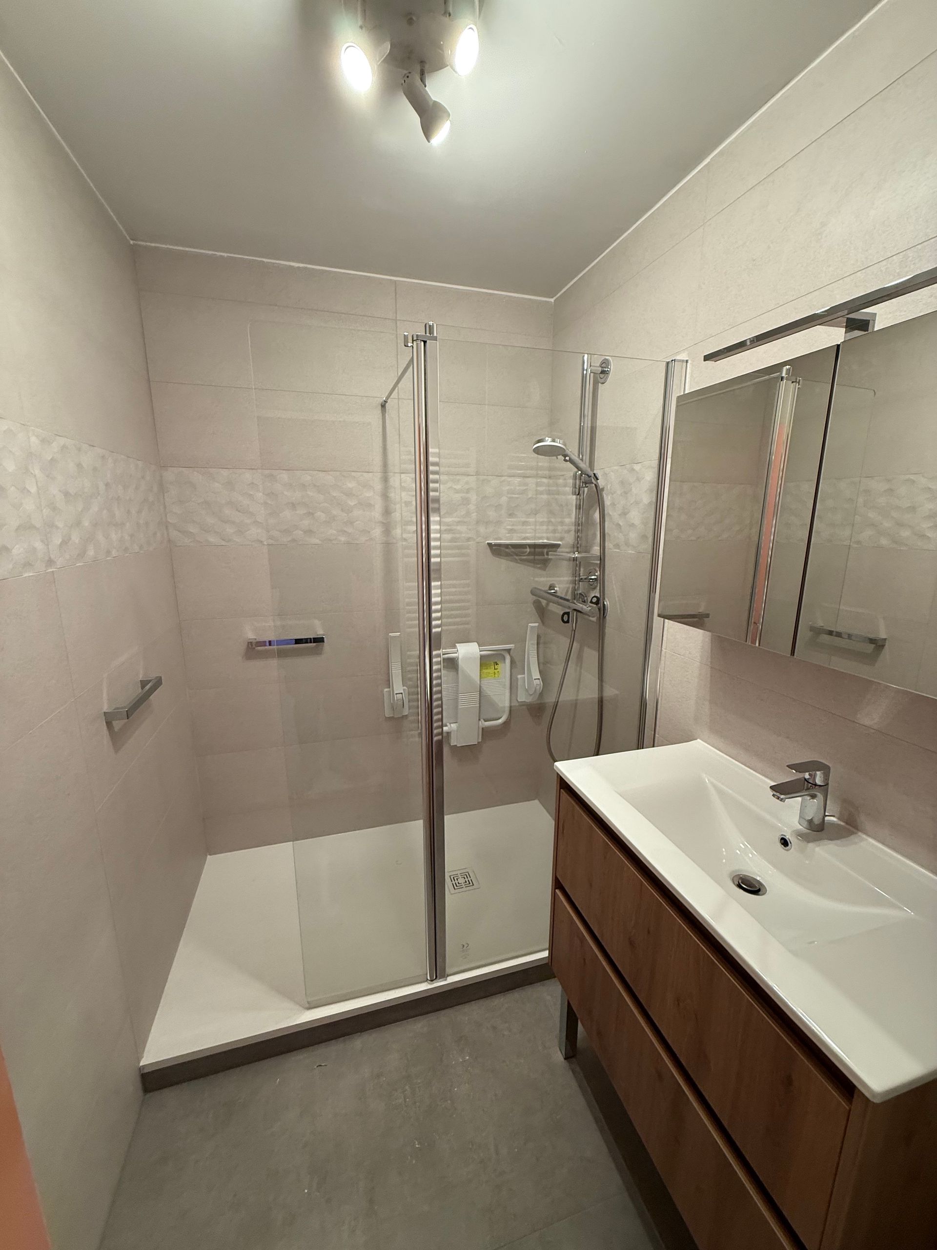 Salle de bains avec douche en verre, lavabo blanc, vanité en bois et murs rose clair.