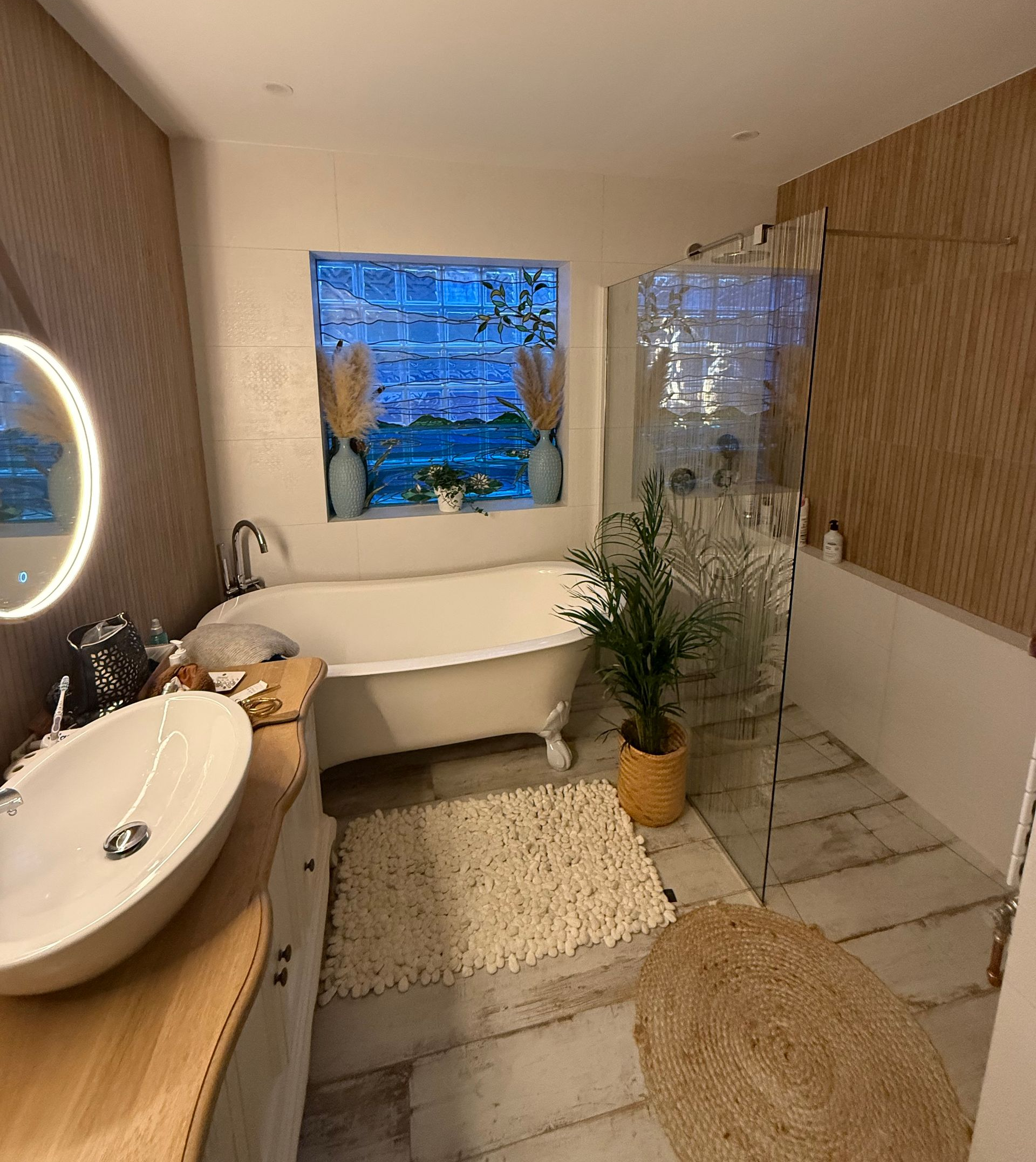 Salle de bains avec baignoire blanche sur pieds, éléments en bois et porte de douche en verre dépoli.