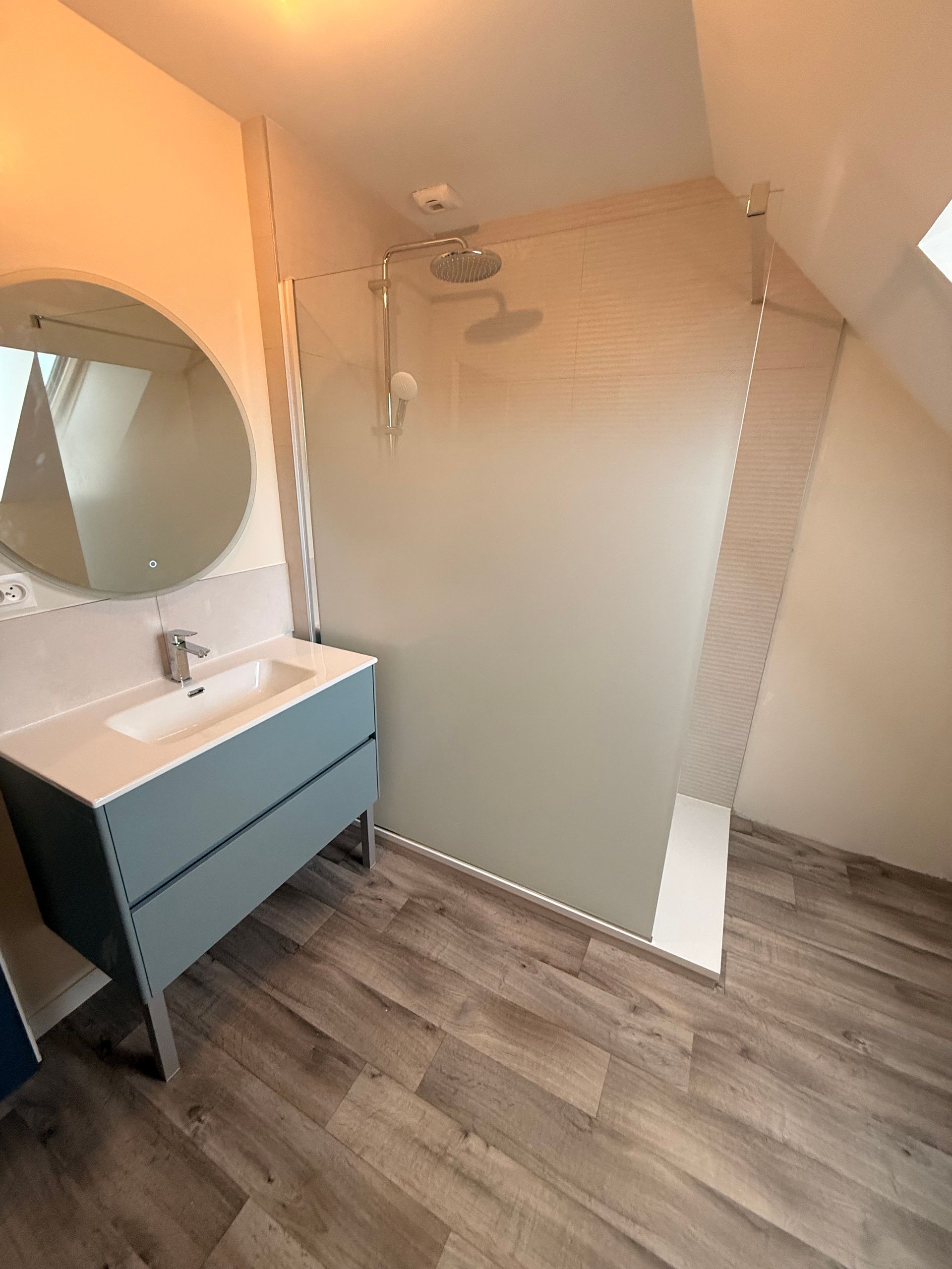 Salle de bains blanche moderne avec douche à cadre noir, miroir rond et lavabo.