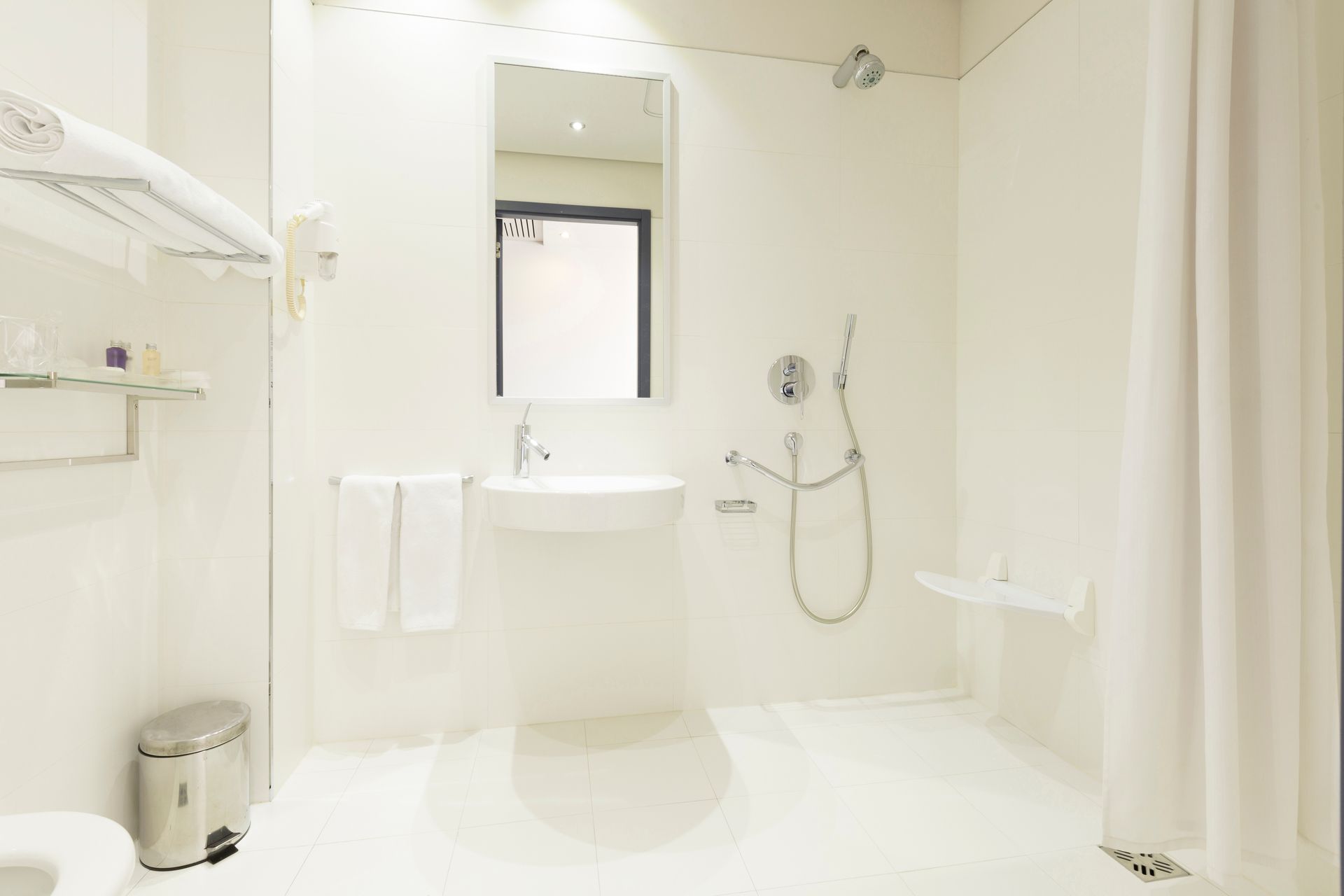 Salle de bains blanche accessible avec lavabo, douche et barre d'appui.