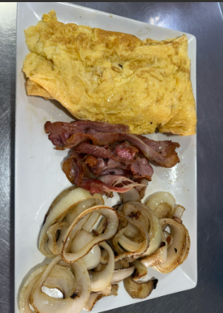 Un plato blanco cubierto con huevos, tocino y cebollas.